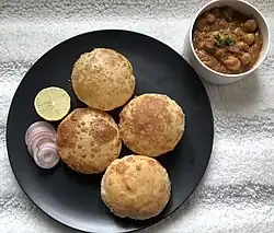 A plate of bhature next to a bowl of chickpea curry
