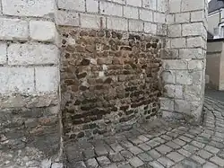 Color photograph of a wall with the first courses made of small brown rubble stones.