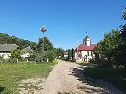 photo of a road in Zavallia during warm months, depicting a church on the right, and houses on the left with a pole hosting a stork nest