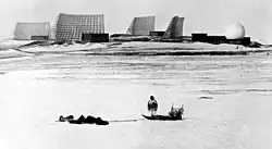 A [[Greenlandic Inuit]] man with a dog sled looks at Thule Site J in 1966.