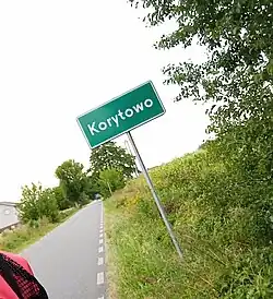 Photograph of the village's roadsign taken at a Dutch angle, 2022