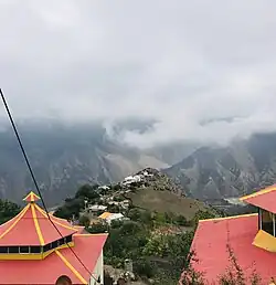 Picture of houses in a valley between two treed mountains; clouds in the sky; buildings with red roofs in the foreground