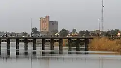 A landscape image of a bridge, with buildings in the background, and a calm river below the bridge.