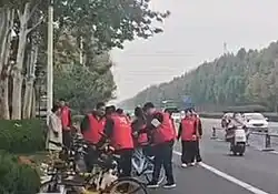 People in vests standing next to bicycles on the side of the road.