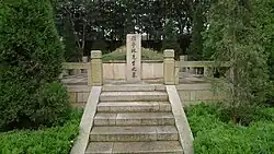 A photo of Gu Yanwu's grave, taking the form of a stele in front of a earthen mound. It is surrounded by foliage, with a stone stairway leading up to it.