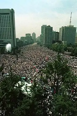 A aerial color photo of massive crowds carrying a few banners and flags, gathered in downtown Seoul and filling the streets as far as the camera can capture.