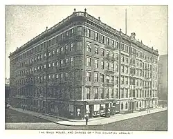 Black and white photo of an urban six-story Victorian commercial building of brick and cast iron on a street corner. The facade to the left is 23 bays wide, to the right is 18, plus a rounded corner one bay wide.