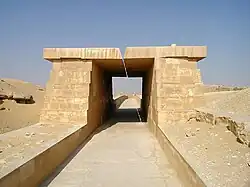 A paved way of white limestone covered with a roof made of massive stone blocks resting on equally massive walls.