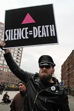 An ACT UP member in 2017, displaying the organization's trademark protest sign with an inverted, upward-pointing pink triangle.