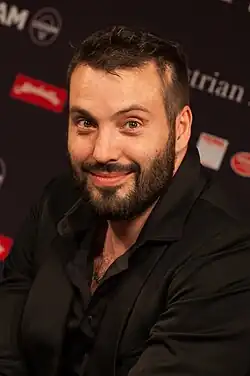 close-up of Václav Bárta wearing an open-necked black shirt and black blazer, smiling broadly at camera