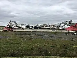A collapsed airport hangar with a couple planes scattered above it