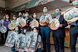 A line of people holding up signs with photos of Mikan in various positions, as well as one holding a curled up Mikan