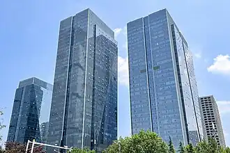 Two skyscrapers standing side by side against a blue sky, two more skyscrapers can be seen in the background as well as some trees in the foreground