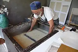 Screening pulp slurry. In background, drying sheets