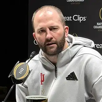 A football coach speaks in front of a microphone.