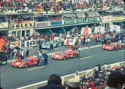 Cars being pushed into place before the race start. Three Scuderia Ferrari 512 S are visible in the foreground, with the Porsche 917s of Gulf, Martini and Porsche Salzburg behind them.