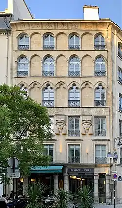 Stone building facade with rows of arched windows, carved Egyptian-style heads, and hieroglyphic frieze above entrance