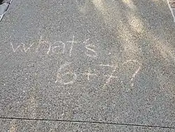 A photo of a sidewalk with chalk writing that reads "What's 6+7?"