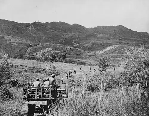 A marine tractor, loaded with ammunition and water, follows Marines along a road leading to the front lines.