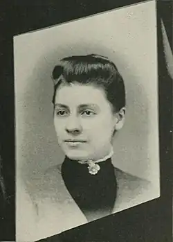 19th-century B&W portrait photo of a woman with her hair in an up-do, wearing a dark, fitted blouse.