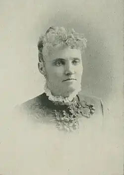 B&W portrait photo of a middle-aged woman wearing a dark, high-collared blouse with her hair in an up-do.