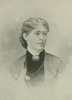 B&W portrait photo of a middle-aged woman wearing a dark, high-collared blouse with her hair in an up-do.