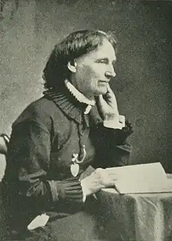 19th-century B&W portrait photo of a woman with her hair in an up-do, wearing a dark, fitted blouse.