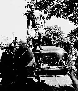 Black and white photo of a man in Nazi uniform standing in front of a car