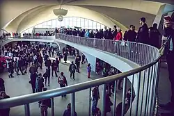 The footbridge on the upper level, spanning above the intermediate level. There are large crowds both on the footbridge and on the intermediate level below.