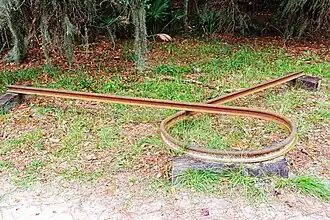 A rusted railroad rail bent into a loop and propped up on wood blocks