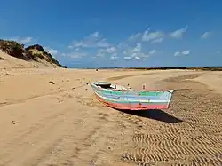 A small, weathered wooden fishing boat resting on a wide sandy beach on Bazaruto Island under a clear blue sky.