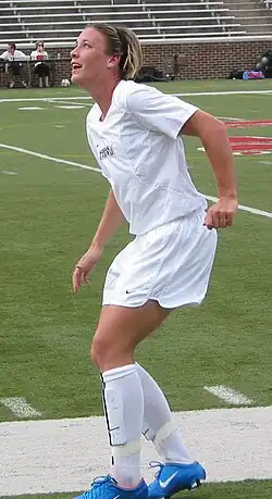Wambach wearing a white uniform by a soccer field.