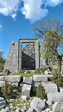 Photograph of a ruin showing a stone door frame, walls and fallen bricks