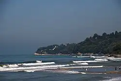 waves hit the beach and there’s a green hill in the distance