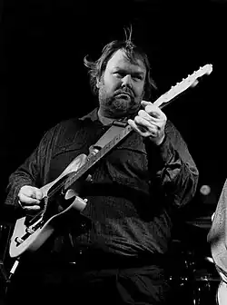 A black-and-white photograph of musician Al Anderson playing an electric guitar