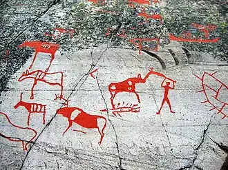 Image of red carvings of animals and people into rock.