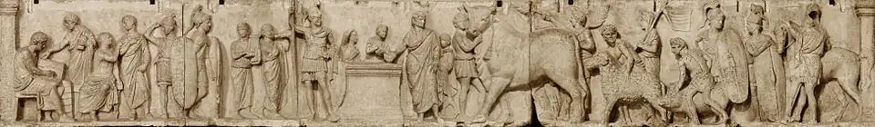 Relief depicts a long continuous scene that may be divided into three main groupings from left. The first is a group of four men wearing togas. Two are seated, and one is writing in a tablet. Two tall military guards divide this group from the central scene of sacrifice. Two musicians, markedly shorter than the soldiers, play a lyre and a horn. An unadorned altar, waist-high, stands in the center. To the viewer's left is the tallest figure in the composition, a military officer wearing a high plumed helmet and holding a long slender spear. standing by an altar. On the other side of the altar a priest, his head ritually covered, extends a libation bowl. A boy attendant pours from a pitcher into the bowl, and to that boy's right is a smaller boy looking on and lifting his right hand to the top of his head, a gesture that appears quizzical to modern viewers but may have some other significance in its Roman context. The priest is accompanied by a third boy close to his left side who stands ready with a towel. The right side of the relief is devoted to the procession of the three animal victims for the suovetaurilia, each led by a young male attendant, barechested, but wearing a short kilt-like garment, with a wreath on his head. The first leads an enormous bull with a tasseled rope dangling from below its left horn. A fourth male attendant in the same attire follows closely on the bull's hindquarter, waving a palm branch in each hand. The attendant bringing the ram is followed by another veiled figure carrying a pole from which a banner unfurls. The attendant herding the pig is followed by another soldier bearing a long shield and looking back at another whose shield rests on the ground, covering most of his body. The last figure is a cavalryman, back turned to the viewer, next to his horse.