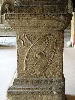 Photograph of an ancient stone altar with a carved circular shield and spear design. The weathered surface suggests historical significance.