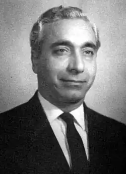 black-and-white image of Amin al-Hafez wearing a light shirt and dark suit with tie, smiling and looking left of camera