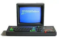 Photograph of a personal microcomputer. A colour monitor sits behind a computer keyboard, both made with black matte plastic.