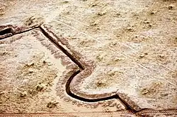 An aerial view of a section of Iraqi trench line abandoned during Operation Desert Storm, image shows a dark trench line in a barren desert environment