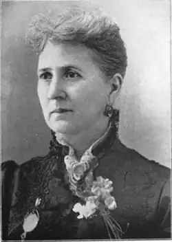 19th-century B&W portrait photo of a woman with her hair in an up-do, wearing a dark, fitted blouse.