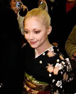 blurry image of Anna Tsuchiya in a crowd of people, wearing a dark kimono, smiling and looking slightly down of camera