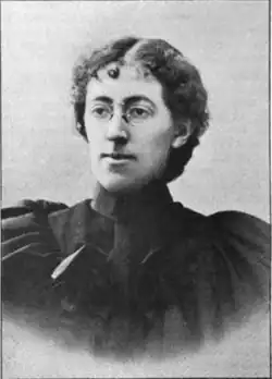 19th-century B&W portrait photo of a woman with her hair in an up-do, wearing a dark, fitted blouse.