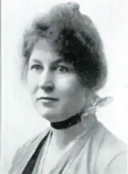 A white woman with frizzy dark hair in an updo, wearing a black velvet choker