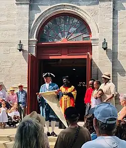 A man in a historic costume from early colonial times with bystanders in front of the doors of the church St. Michel in Vaudreuil-Dorion