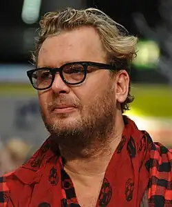 close-up of Antti Juhanpoika Jokinen wearing a red-and-black plaid shirt and a red-and-black patterned scarf, looking to the right of camera