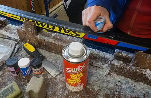 Application of grip wax to a classic cross-country ski, using a canister of wax, like those shown in the left foreground