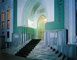 Grand entrance with marble steps leading to an ornate golden door framed by arched turquoise walls and glowing lanterns