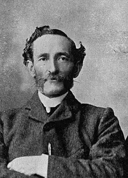 Portrait photograph of a man with a moustache wearing a suit